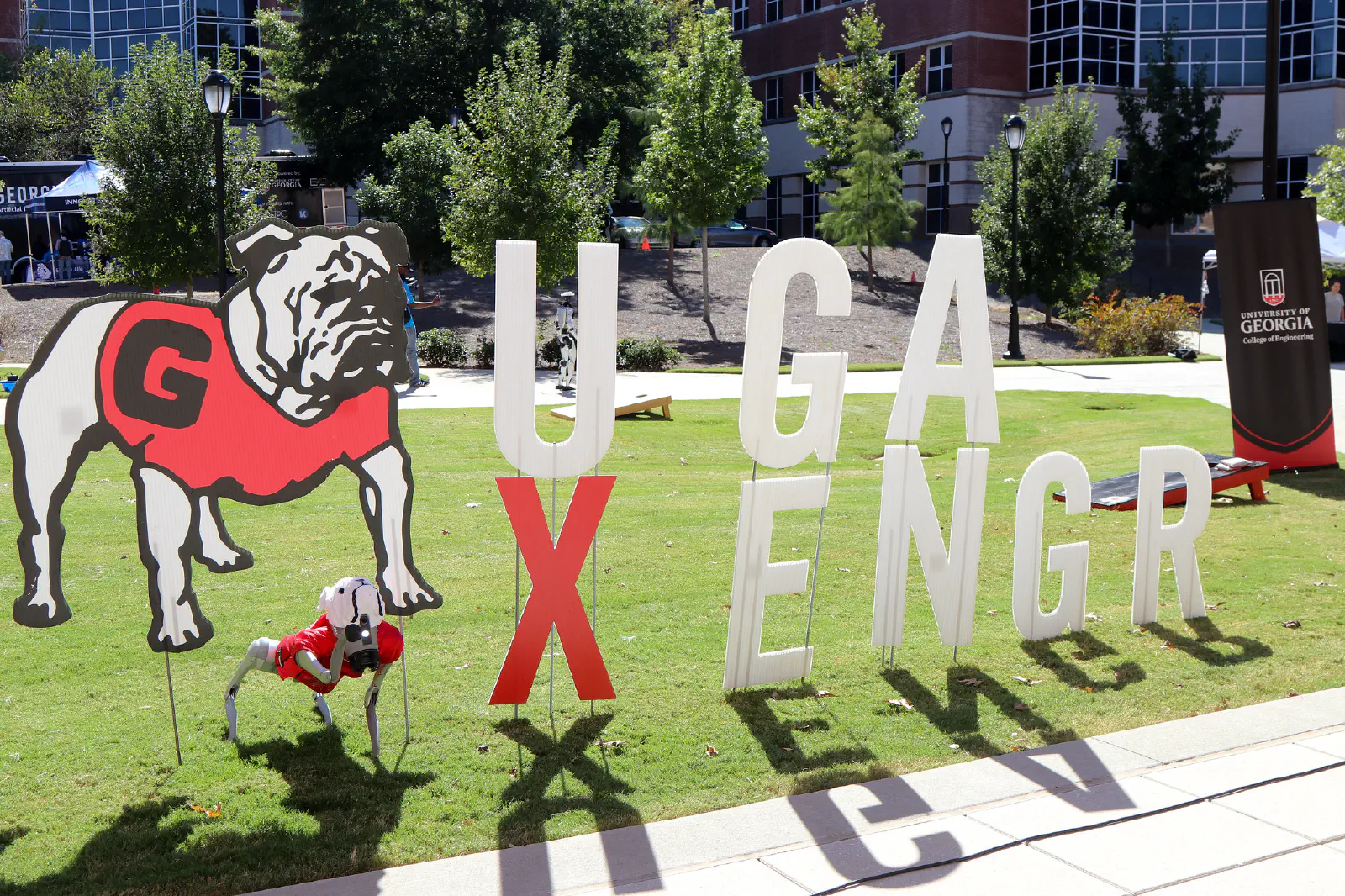 Robot dog standing outside on the campus lawn in front of large letters that say UGA XENGR